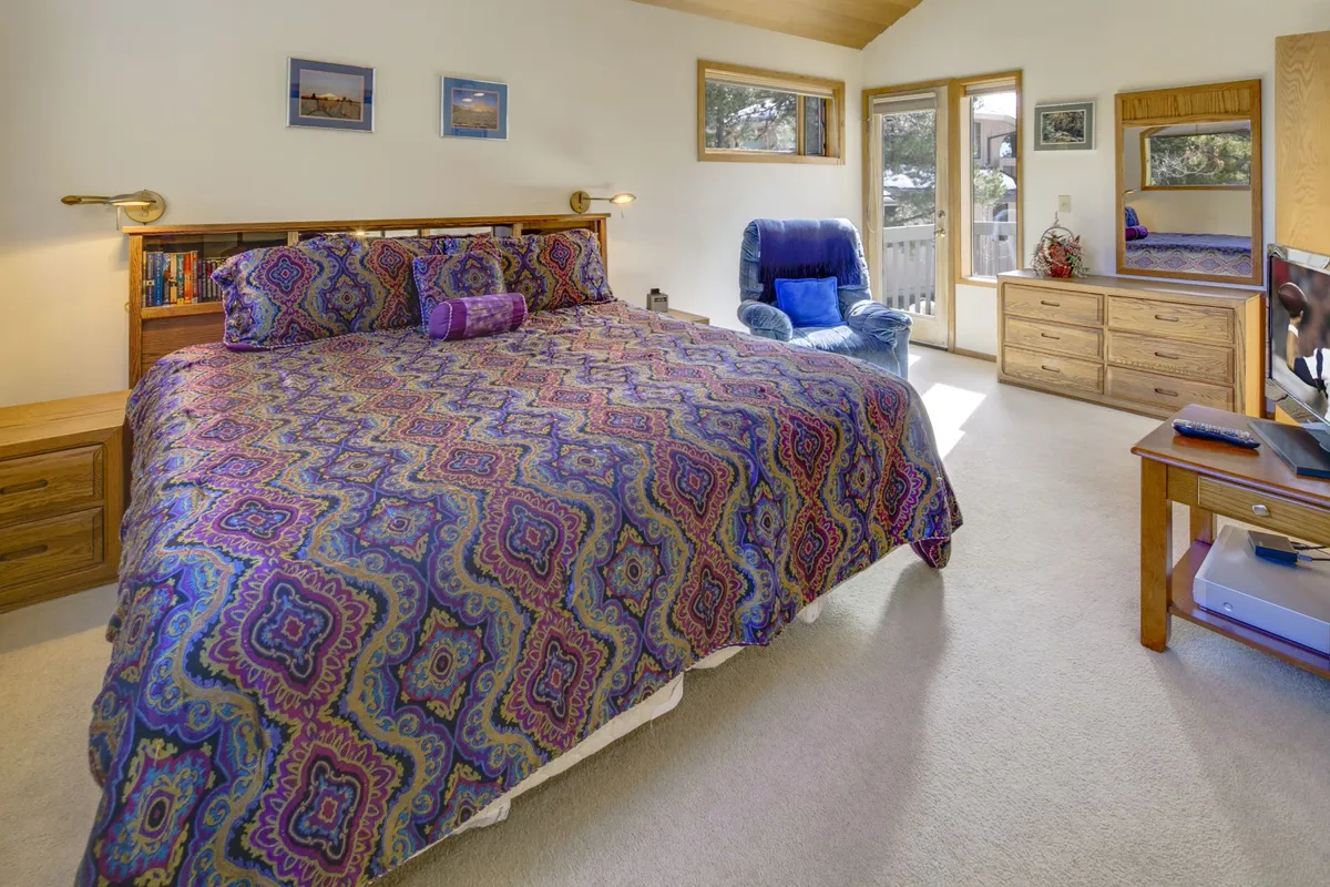 A spacious bedroom with a large bed adorned with colorful bedding, a blue chair for relaxation, and a dresser with a mirror. Soft natural light creates a tranquil and peaceful mood, reinforcing a sense of comfort.