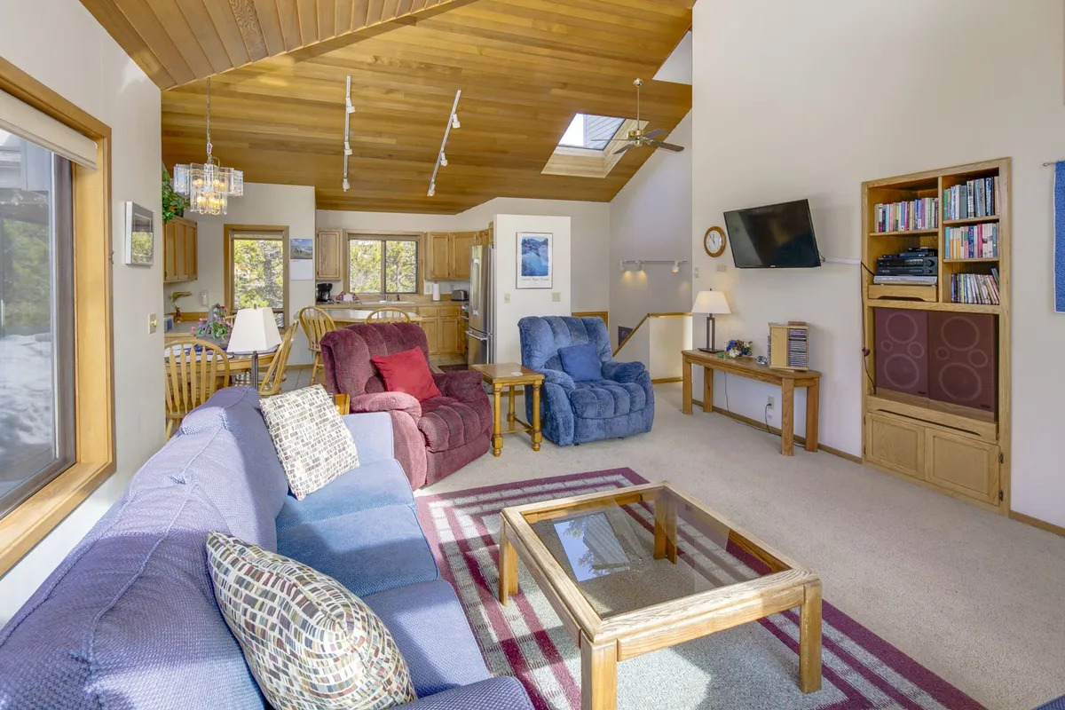 A cozy living area featuring a sofa, recliners, a coffee table, and a TV, arranged for group gatherings or relaxation. The room's layout suggests comfort and flexibility for guests to unwind together or use the sleeper sofa as needed.
