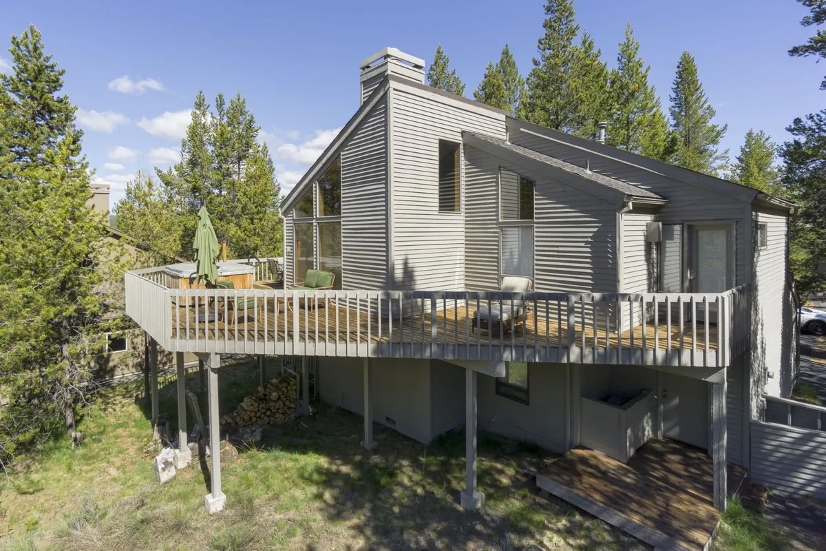 A broad deck surrounded by greenery, with views into the home’s living space through large windows. The area is set up for outdoor dining or simply relaxing and enjoying the natural setting, perfectly capturing the indoor-outdoor living that makes the property appealing to pet owners.