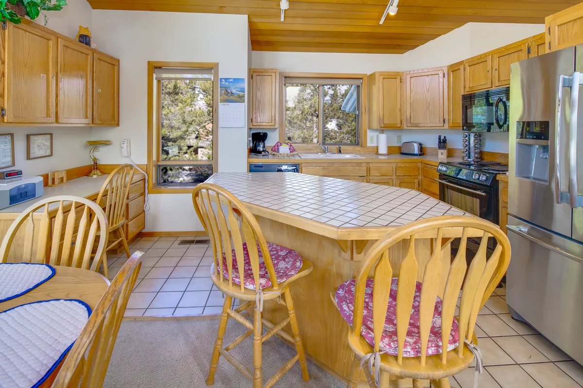 A warm, inviting kitchen with a central island, wooden cabinets, and large windows letting in natural light. The setup encourages cooking together and casual conversations, with plenty of space for multiple people to participate in meal prep or simply gather around.