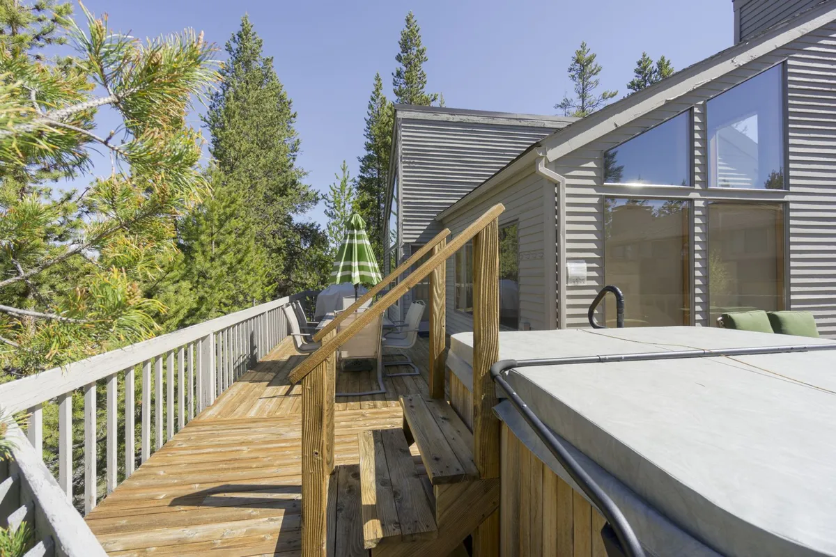 A peaceful outdoor scene featuring a wooden deck with a hot tub, lounge chairs, and green trees in the background. The atmosphere is tranquil and inviting, ideal for spending quality family time outdoors.