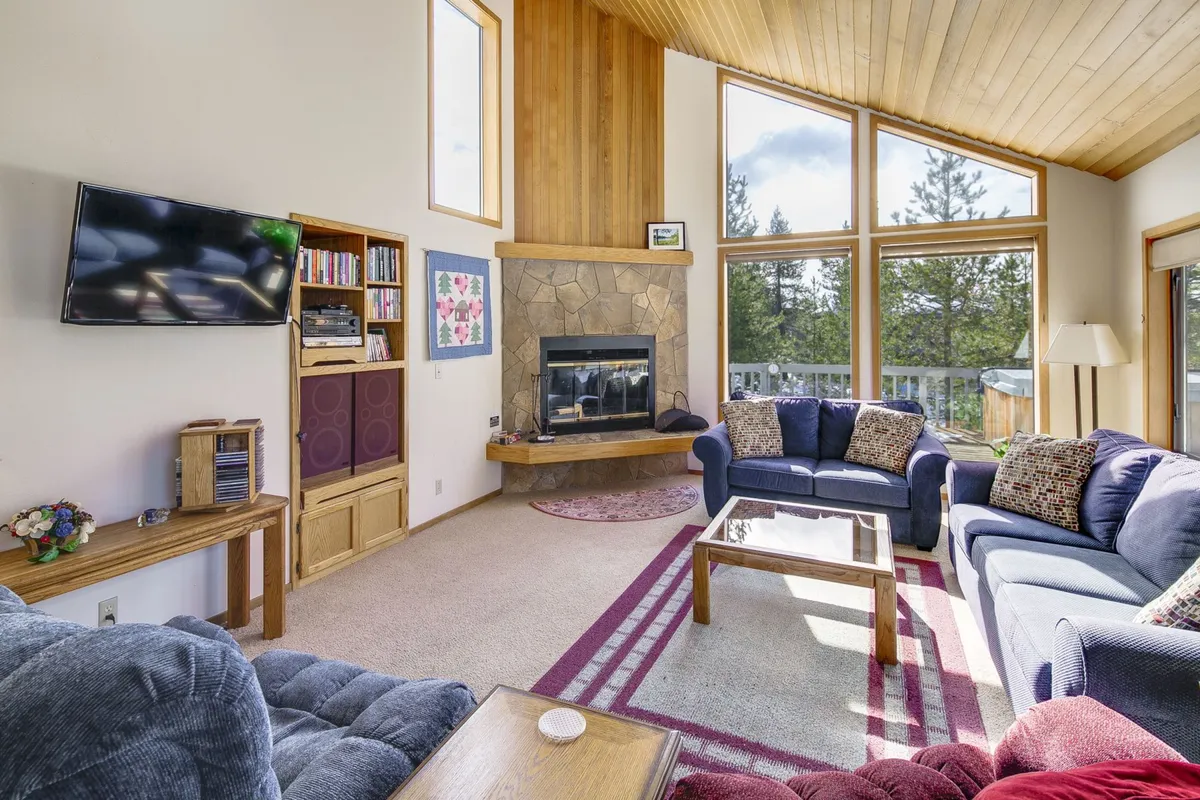 A cozy living room with a prominent fireplace as its centerpiece, surrounded by large windows that flood the space with natural light. The sofa arrangement and coffee table invite relaxation and conversation, while the overall ambiance is warm and inviting.