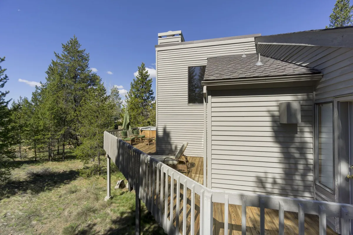 This exterior shot offers a wider view of the home’s deck nestled among tall trees. The space is designed for relaxation and group gatherings, with ample room for family activities and enjoying nature.