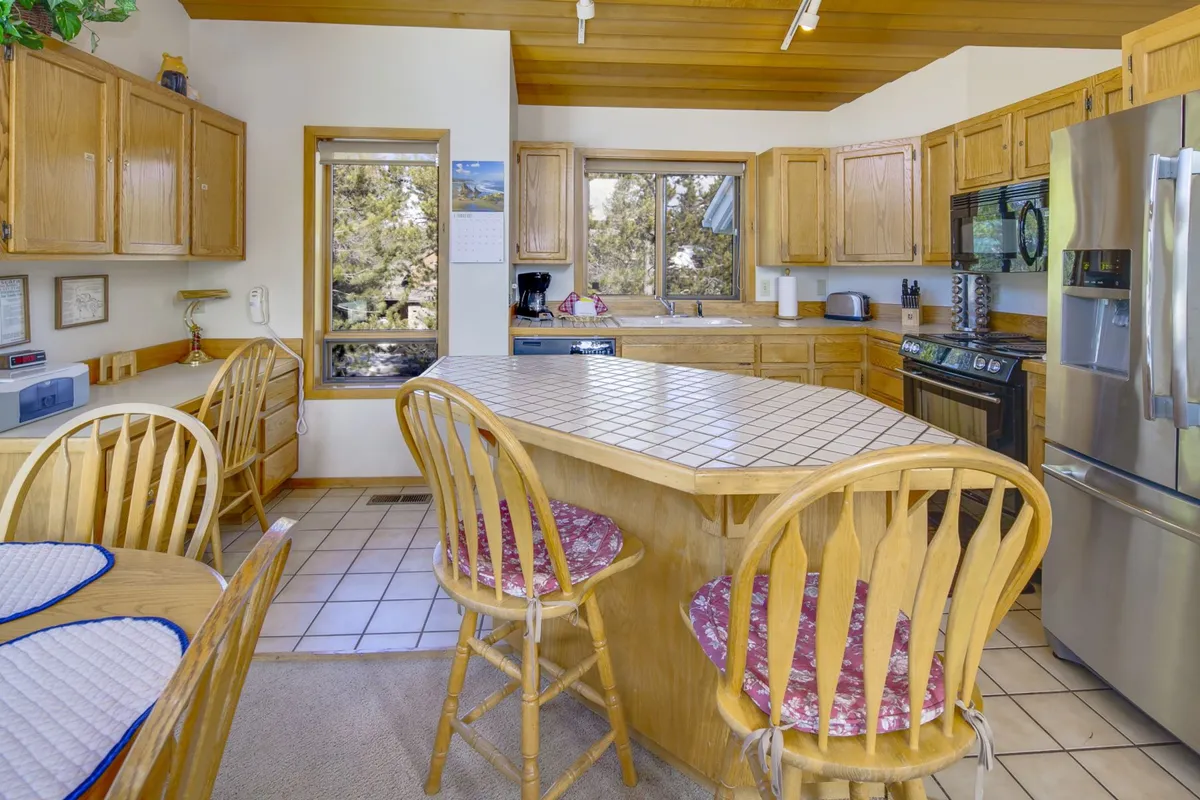 A view of the kitchen island with stainless steel appliances and windows that look out onto nature. The cozy setup invites family gatherings, holiday meal prep, and lingering conversations over coffee or dinner.