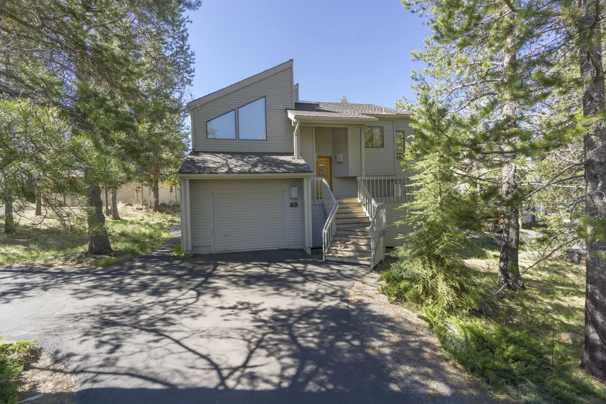 This exterior image highlights the unique architectural design of the house, framed by tall pine trees and a clear blue sky. The scene evokes a sense of tranquility and connection to nature, emphasizing the property's integration with Sunriver's scenic landscape and nearby trails.