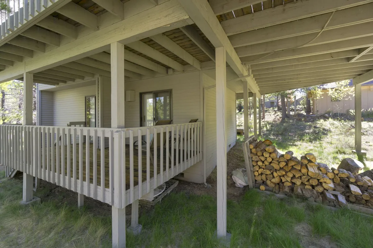 This image features another angle on the exterior deck area, complete with a sturdy railing, a wood pile for cozy fires, and exposed beams. The scene is casual and tranquil, suggesting a place for morning coffee or gathering with friends after an active day. The visible natural surroundings reinforce the sense of connection to the outdoors.