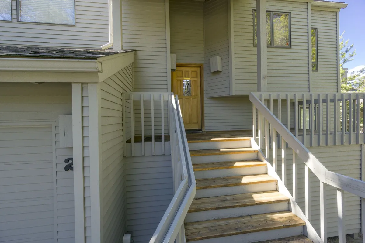 This image shows the welcoming wooden front door, flanked by a staircase and railings. The entryway radiates a friendly first impression and hints at the home’s inviting interior and the adventures waiting just outside. The outdoor setting—with the porch and views—evokes feelings of arrival and anticipation.